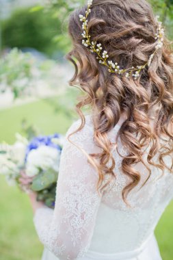 Güzel saç stili ve saçlarında altın aksesuarları olan kıvırcık gelin düğün buketi taşıyor.