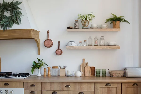 Light wooden kitchen interior with kitchen utensils on the shelves and on the wall. Beautiful kitchen interior design