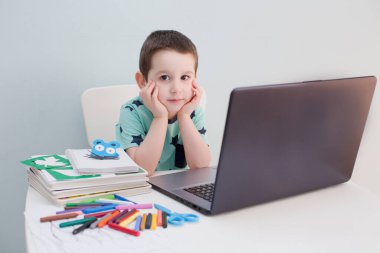 Çevrimiçi eğitim konsepti. Kulaklık takan küçük beyaz bir çocuk internette bilgisayar ve evde eğitim kavramlarıyla ilgili video çalışmaları yapıyor. Anaokulu çevrimiçi çalışması