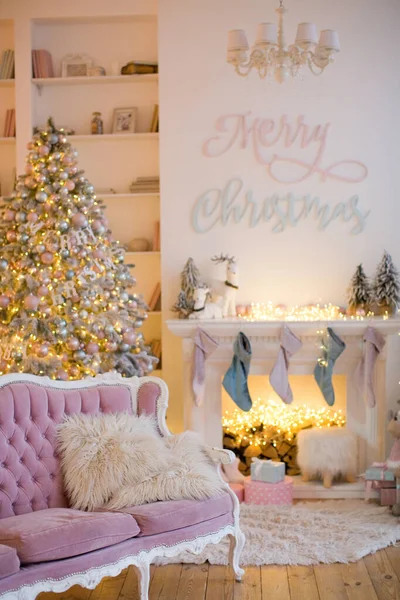 Christmas interior with fireplace, pink sofa, Christmas tree and pink and blue decorations
