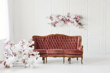 Klasik kahverengi kanepe ve çiçekli duvar dekorasyonu beyaz ahşap duvarlarla aydınlık odada.