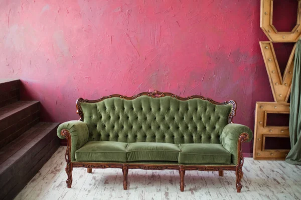 Vintage green sofa in dark loft room with wooden stairs and wooden decorations.