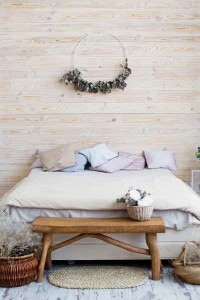 木製の壁と軽いボヘミアンベッドルーム 枕と毛布 木製のバンチとドライフラワーの装飾付きのベッド — ストック写真