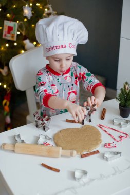 Noel ağacının yanındaki beyaz bir masada ışıklarla Noel kurabiyesi yapan tatlı çocuk. Noel yemeği konsepti