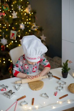 Noel ağacının yanındaki beyaz bir masada ışıklarla Noel kurabiyesi yapan tatlı çocuk. Noel yemeği konsepti