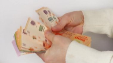 Beyaz kadın eli Arjantin pesolarının yakın plan ve beyaz arkaplanda uzanan banknotlarını sayıyor.