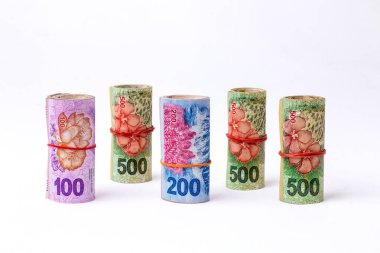 Cash in Argentine peso bills in rolled blocks of 100, 200 and 500 pesos tied with a red elastic band and standing on a white background and free space around.  clipart