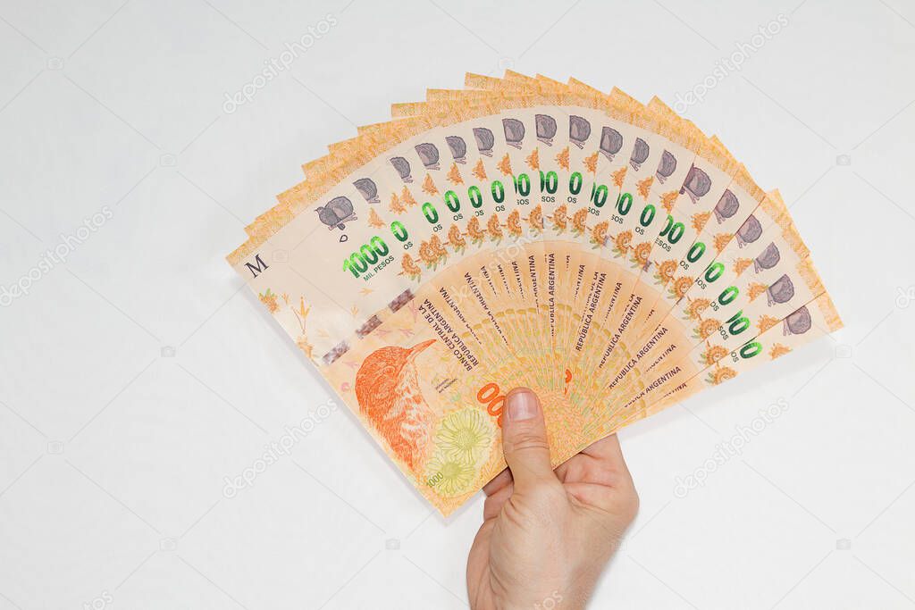 1000 Fan's Argentine peso bills held by the right hand of a Caucasian woman with short natural nails on a white background copy space.