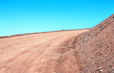 Arjantin 'in And Dağları çölünde, bulutsuz gökyüzünün altında yükselen toprak yol dağ yamacını çevrelemektedir..