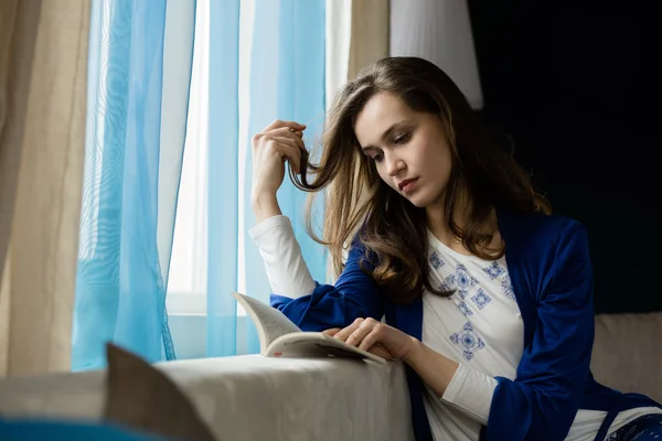 Jonge vrouw leest een boek naast een raam — Stockfoto