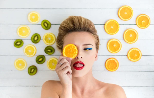 Blonde vrouw leggen naast segmenten van sinaasappel, citroen en kiwi — Stockfoto