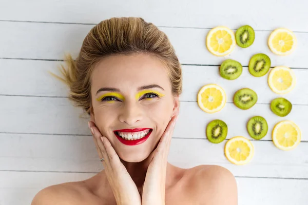 Blonde woman laying next to slices of lemon and kiwi — Stock Photo, Image