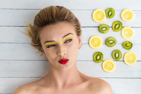 Mulher loira que coloca ao lado de fatias de limão e quivi — Fotografia de Stock