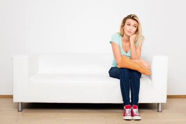 Blonde women sitting on couch with a pillow — Stock Photo, Image