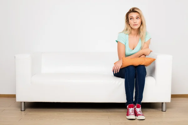 Blond ženy sedí na gauči s polštářem — Stock fotografie