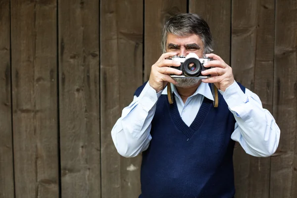 Velho fotógrafo de pé sobre fundo de madeira — Fotografia de Stock