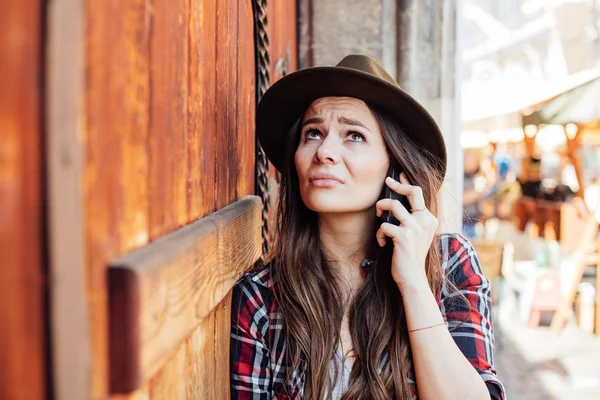 Mujer joven con un sombrero al lado de una vieja puerta de madera hablando en cel — Foto de Stock