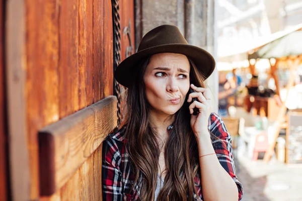 Mujer joven con un sombrero al lado de una vieja puerta de madera hablando en cel — Foto de Stock