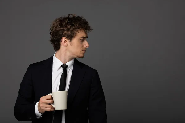 Eleganter Mann im Anzug mit einer Tasse auf grauem Hintergrund — Stockfoto