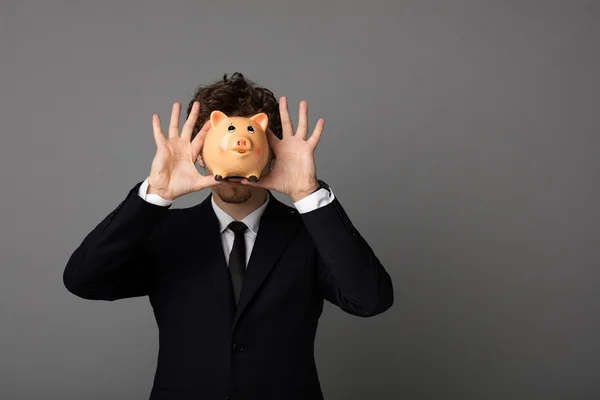 Eleganter Mann mit Sparschwein auf grauem Hintergrund — Stockfoto