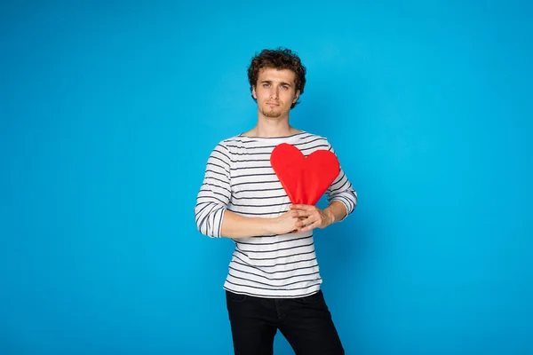Young curly man with red heart on blue background — Stock Photo, Image