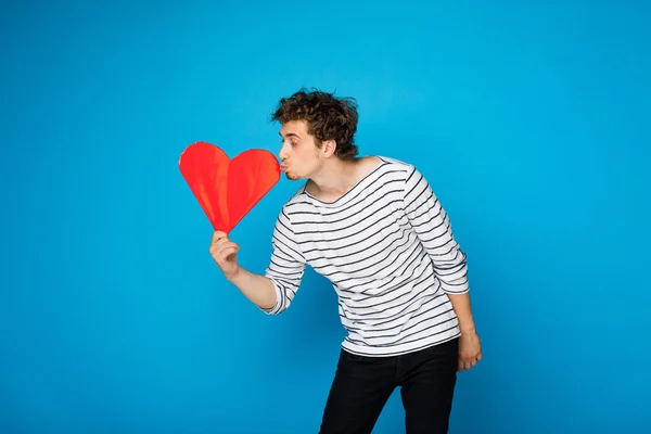 Young curly man with red heart on blue background — Stock Photo, Image