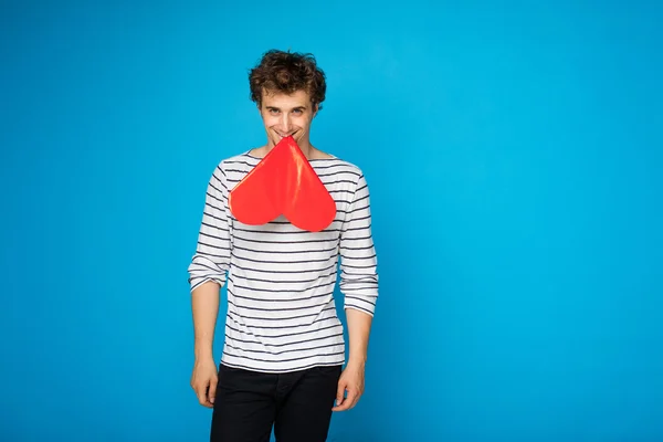 Young curly man with red heart on blue background — Stock Photo, Image