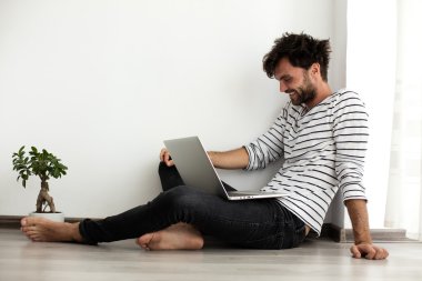 young man sitting down on the floor with laptop and a plant next