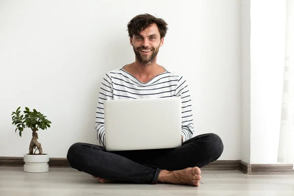 Junger Mann setzt sich mit Laptop und Pflanze neben sich auf den Boden — Stockfoto