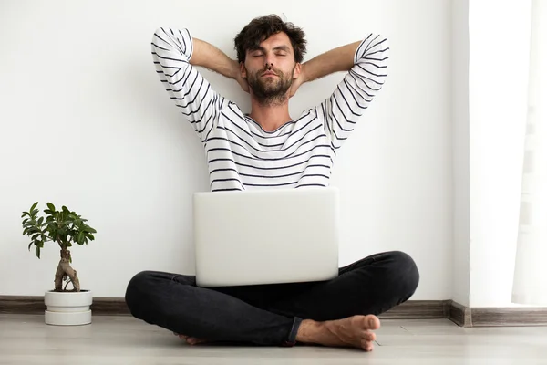 Junger Mann setzt sich mit Laptop und Pflanze neben sich auf den Boden — Stockfoto