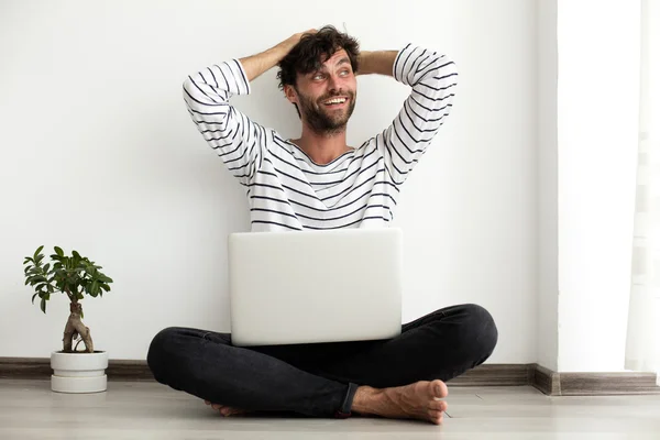 Junger Mann setzt sich mit Laptop und Pflanze neben sich auf den Boden — Stockfoto