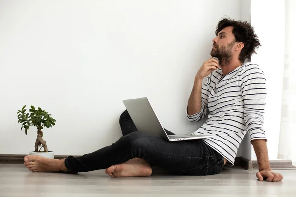 Junger Mann setzt sich mit Laptop und Pflanze neben sich auf den Boden — Stockfoto