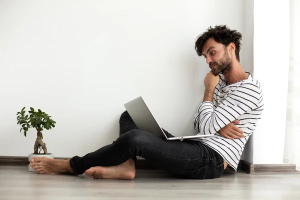 Junger Mann setzt sich mit Laptop und Pflanze neben sich auf den Boden — Stockfoto