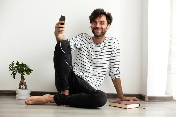 Sitthing mladý muž na podlaze se sluchátky v uších a wi — Stock fotografie