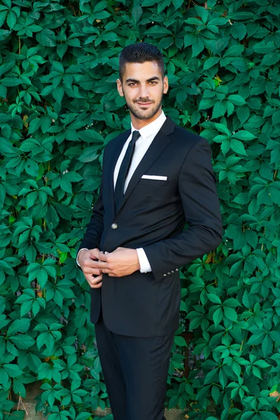 Elegante uomo d'affari in piedi su sfondo foglie — Foto Stock