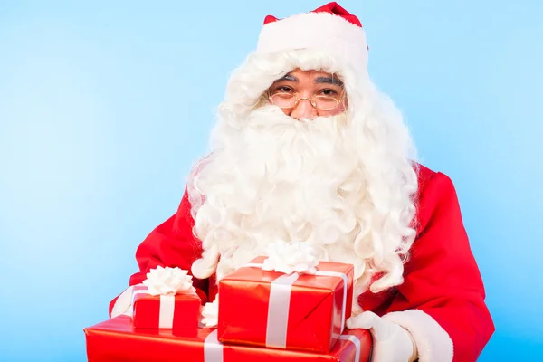 Weihnachtsmann mit Geschenken auf Händen auf blauem Hintergrund — Stockfoto