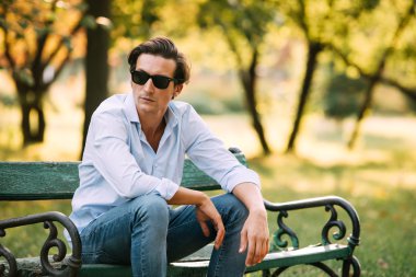 attractive man sitting alone on the bench with cellphone