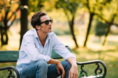 attractive man sitting alone on the bench with cellphone