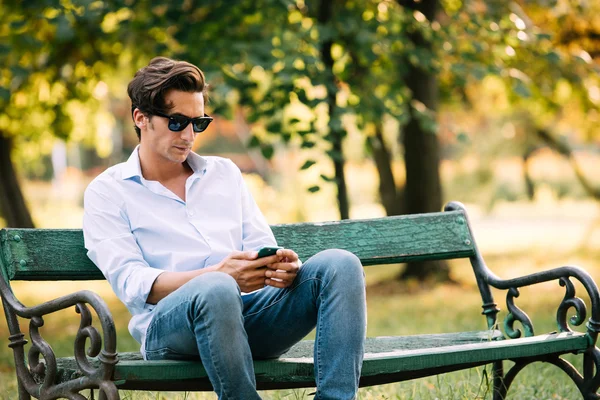 attractive man sitting alone on the bench with cellphone