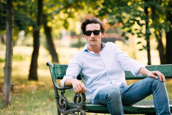 Uomo attraente seduto da solo sulla panchina con il cellulare — Foto Stock