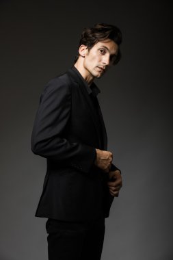 Siyah takım elbiseli çekici bir adam karanlık arka planda rol yapıyor.