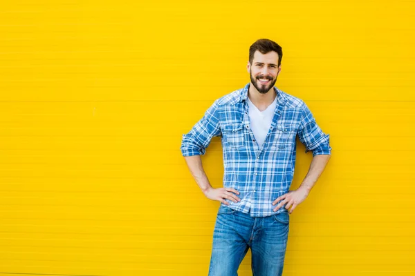 Giovane uomo felice in piedi contro un muro giallo — Foto Stock