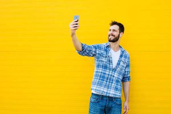 Jeune homme beau avec écouteurs sur le mur jaune — Photo