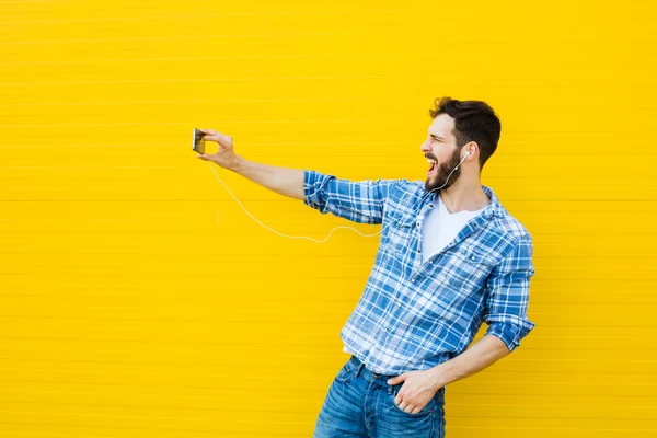 Jeune homme beau avec écouteurs sur le mur jaune — Photo
