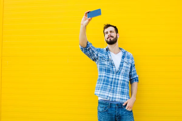 Jeune homme beau avec écouteurs sur le mur jaune — Photo