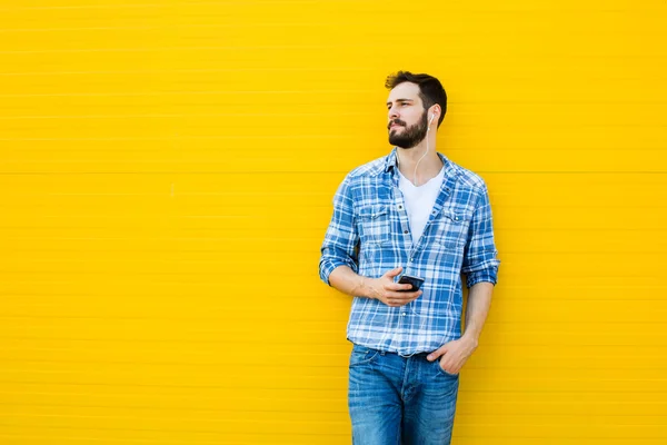 Mladý pohledný muž se sluchátky na žluté zdi — Stock fotografie
