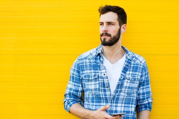Junger schöner Mann mit Kopfhörern an gelber Wand — Stockfoto