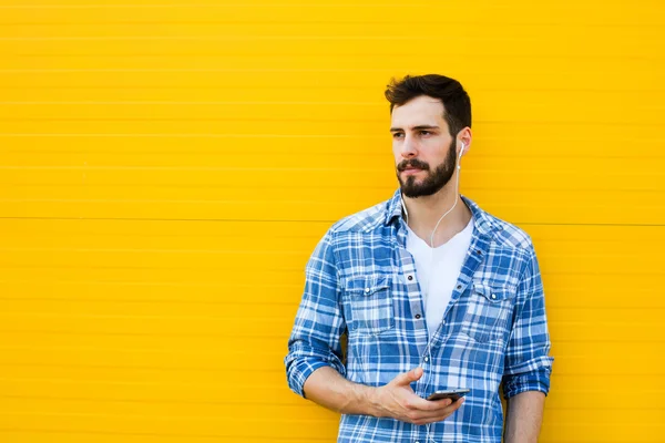 Jovem homem bonito com fones de ouvido na parede amarela — Fotografia de Stock