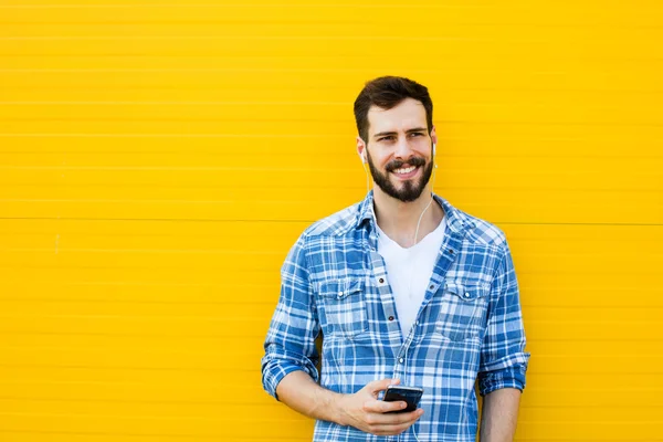 Joven hombre guapo con auriculares en la pared amarilla — Foto de Stock