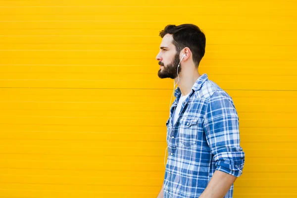 Jeune homme beau avec écouteurs sur le mur jaune — Photo